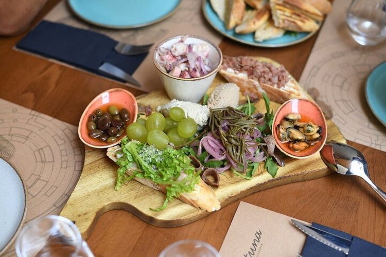 A wooden board with mixed appetizers in Zadar grapes, olives, bread, cheese, pickled onions, seafood, greens, and octopus salad..jpg