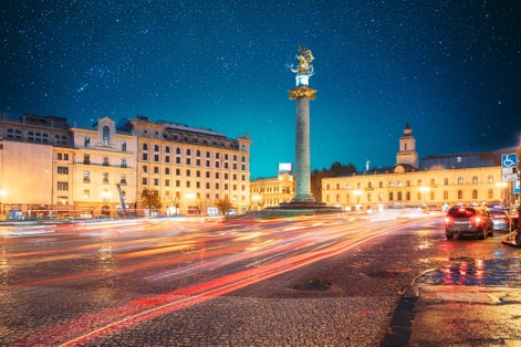 photo of Amazing Bold Bright Blue Starry Sky Gradient Above Liberty Monument Depicting St George Slaying the Dragon and Tbilisi City Hall in Freedom Square in City Center in Georgia.