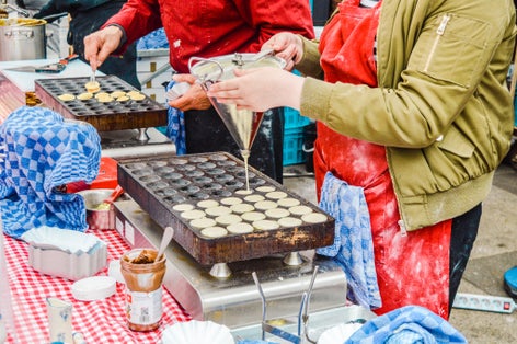 Photo of Two vendors prepare Traditional Dutch poffertjes at the Albert Cuyp market in Amsterdam.