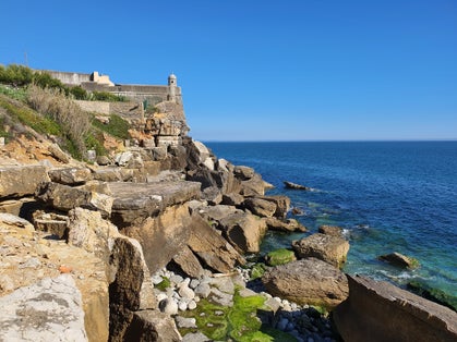 Rocky beach and medieval Fort or Forte de Santo António da Barra. Atlantic Ocean shore and blue sky background.