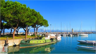 Photo of Old harbour Porto Vecchio with motor boats on turquoise water, green trees and traditional buildings in historical centre of Desenzano del Garda town, Northern Italy.