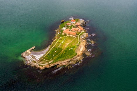 photo of view of Saint Anastasia Island in Burgas bay, Black Sea, Bulgaria. Lighthouse tower and old wooden buildings on rocky coast,Burgas Bulgaria.