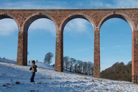 Photo of Man stands in front of Leaderfoot Viaduct in the Scottish Borders on a snowy day .