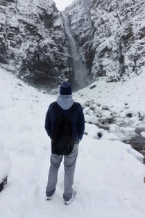 photo of man watching the Njupeskär waterfall in beautiful winter landcape in Sweden.