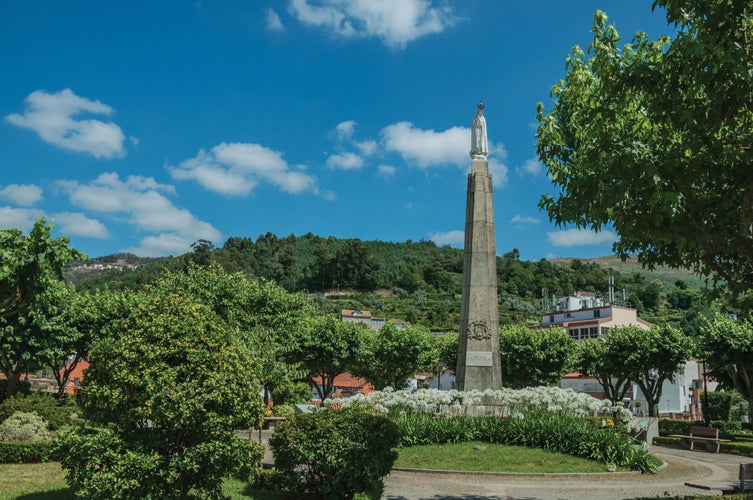 Marble statue of Our Lady on stone pillory at flowered garden, in a sunny day at Seia. On foothill mountains, this friendly town in eastern Portugal is also known for its delicious artisanal cheese.