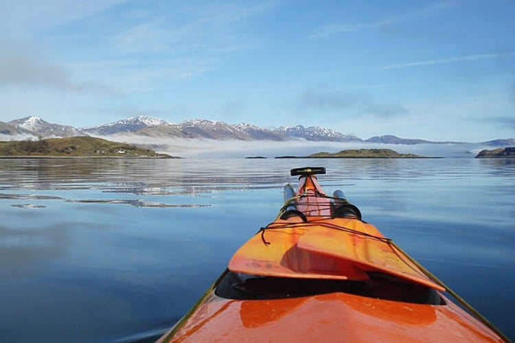 A sea kayak rests on calm waters around the Isle of Lismore on Scotland-s west coast, as morning fog lifts to reveal snow-capped mountains in the distance.jpg