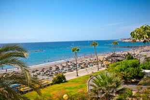 photo of aerial shot of Costa Adeje area, South Tenerife, Spain. Captured at golden hour, warm and vivid sunset colors. Luxury hotels, villas and restaurants behind the beach.