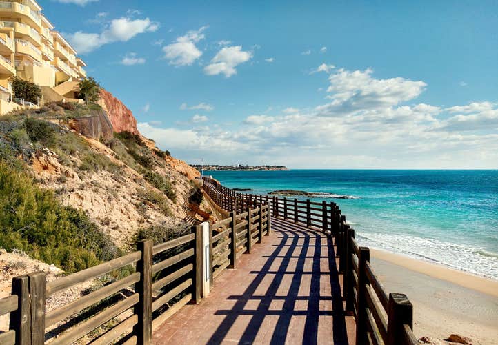 Photo of wooden boardwalk with a view of beautiful beach in Dehesa de Campoamor Alicante province, Costa Blanca, Spain.