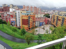 Photo of aerial view of Bilbao, Spain city downtown with a Nevion River, Zubizuri Bridge and promenade. Mountain at the background, with clear blue sky.