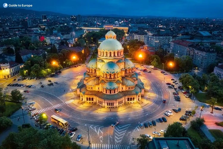 Alexander Nevsky Cathedral in Sofia, Bulgaria, at night, surrounded by city lights, parked cars, and urban architecture in the background..jpg