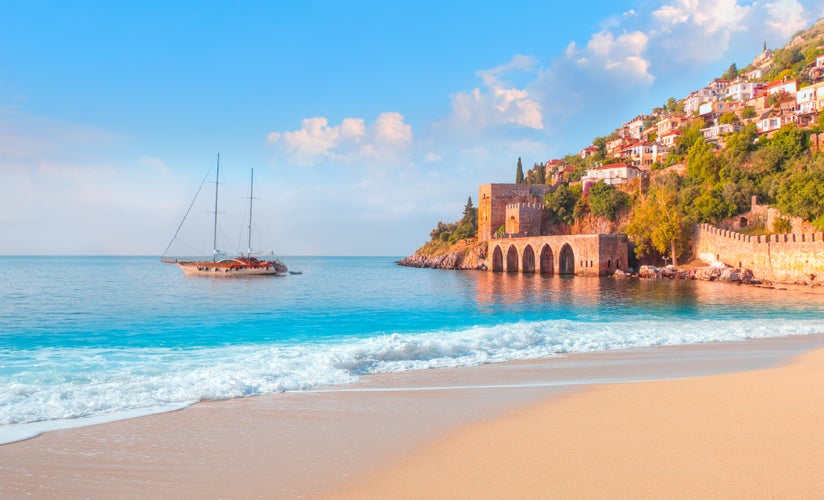 Photo of beautiful sandy beach and soft turqoise Mediterranean sea wave, Landscape of ancient shipyard near of Kizil Kule tower - Alanya peninsula, Turkey.