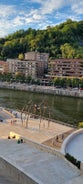 Photo of aerial view of Bilbao, Spain city downtown with a Nevion River, Zubizuri Bridge and promenade. Mountain at the background, with clear blue sky.