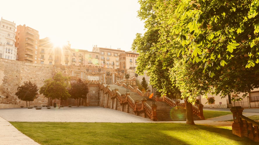 photo of view of Sunrise view of Escalinata del Ovalo and surrounding plaza in Teruel, Spain, with lush greenery.