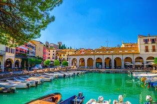 Photo of Old harbour Porto Vecchio with motor boats on turquoise water, green trees and traditional buildings in historical centre of Desenzano del Garda town, Northern Italy.