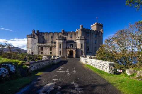 Photo of Horizontal wide angle view of beautiful Scottish Castle, bridge entrance, Dunvegan Castle Isle of Skye, Scotland. Sunny day with bright blue sky. 