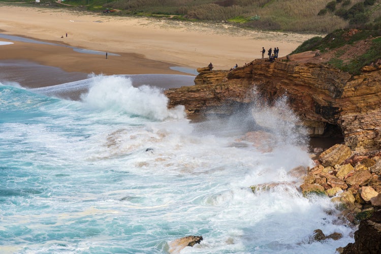 People standing at the edge of a rough cliff facing big waves in Nazare.jpg