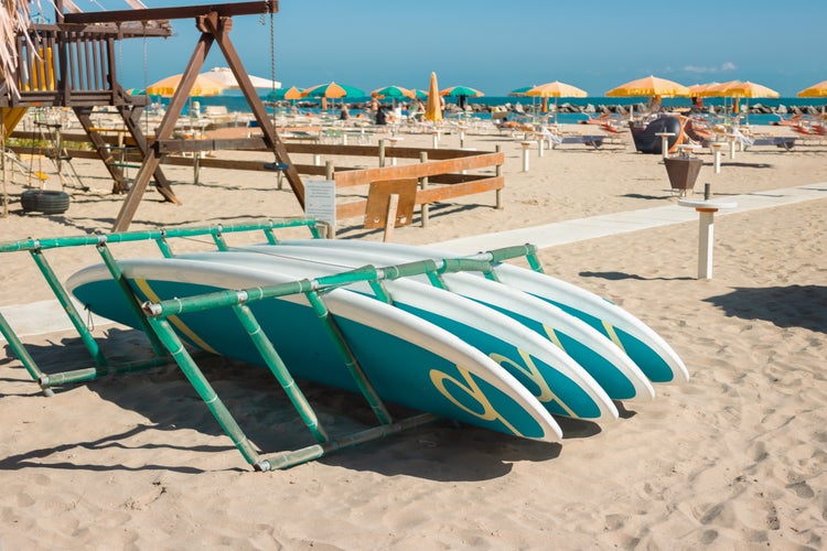 Photo of Surfboard on sandy beach at beach Viserbella Italy on background of beach umbrellas and sunbeds.