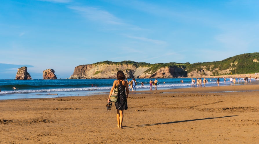 A young brunette in a black dress and sunglasses walking along the beach in Hendaye, French Basque country, France. 