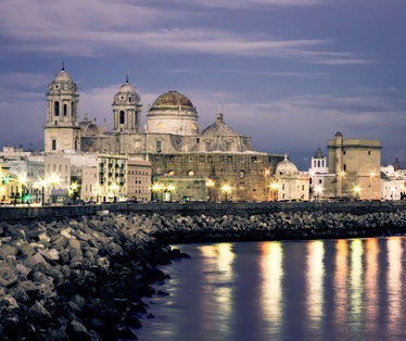 photo of beautiful view at night of the cathedral of Cadiz called cathedral de Santa Cruz with its 2 towers and its golden dome and ocean in Cadiz Andalusia Spain Europe.