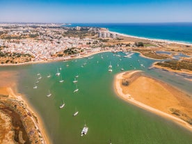 Photo of beautiful aerial view of the sandy beach surrounded by typical white houses in a sunny spring day, Carvoeiro, Lagoa, Algarve, Portugal.